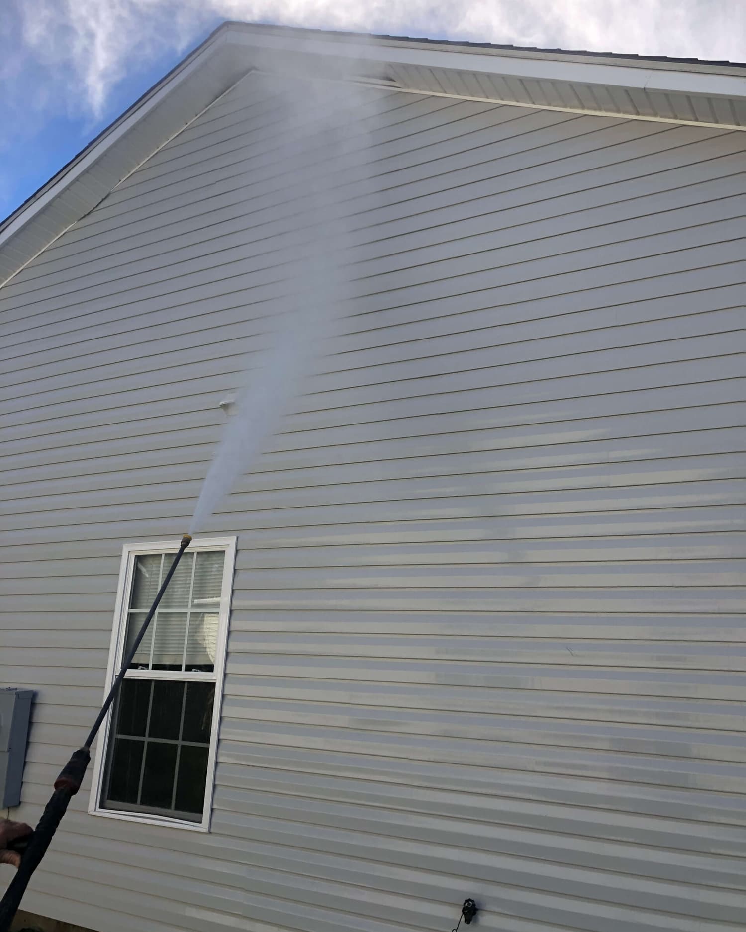 A house being pressure washed by S&S, the wand and spray arc cutting the mildew off the siding